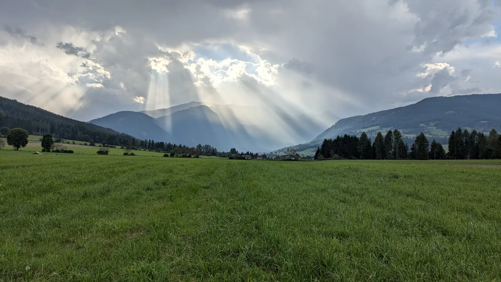 Sun rays breaking through clouds over a wide green field