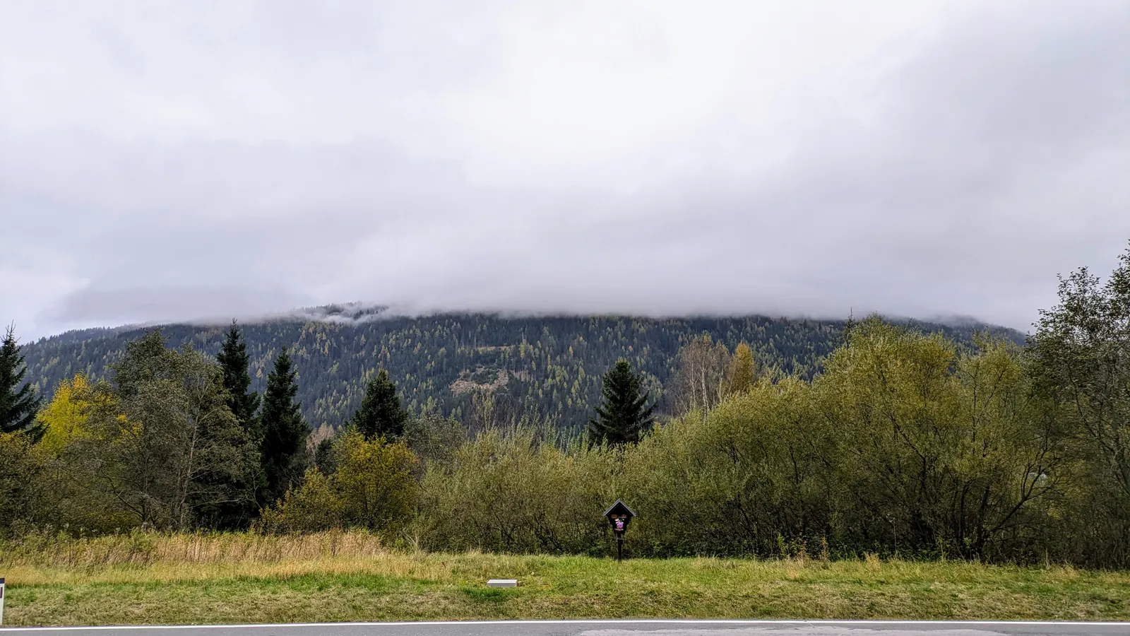 Autumn field and wooded hills under low clouds