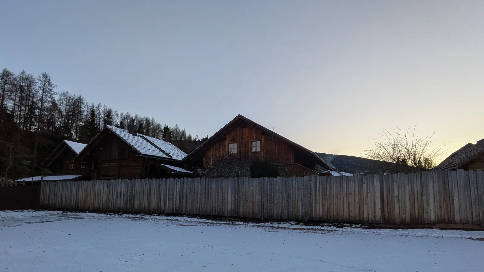 Winter village view with wooden building and fenced snowfield