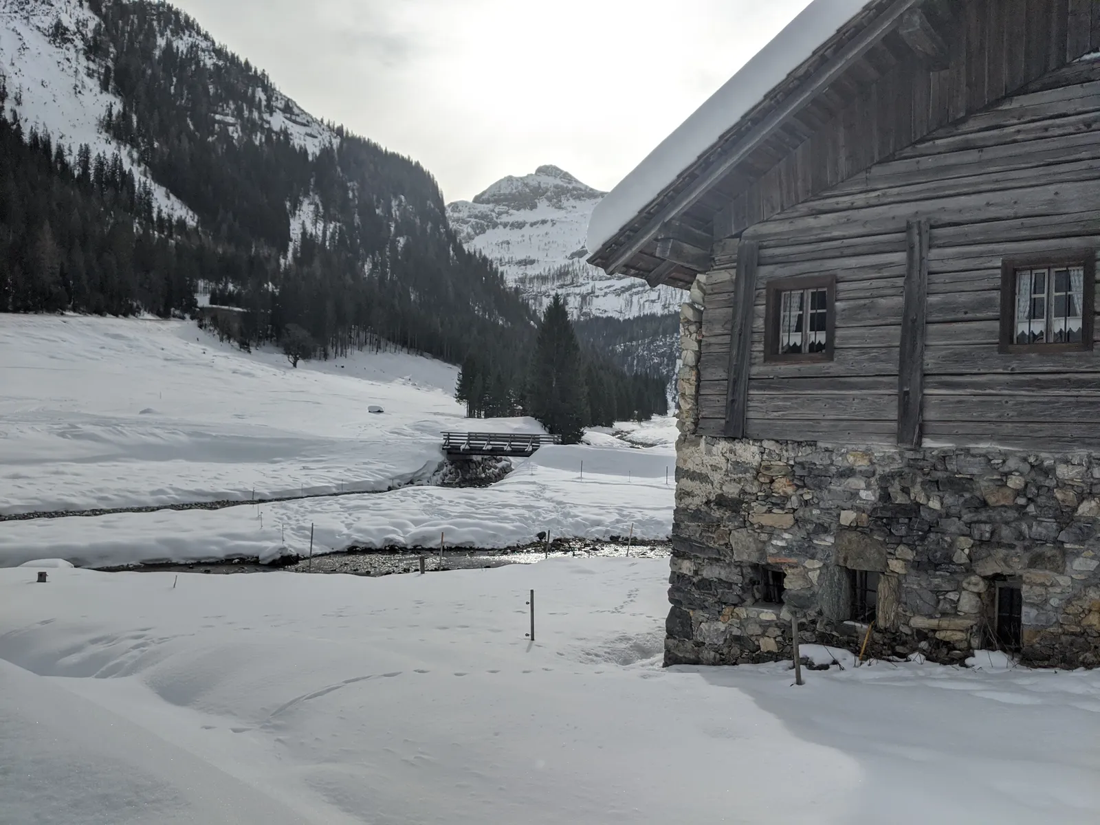 Snow-covered alpine hut beside a winter valley