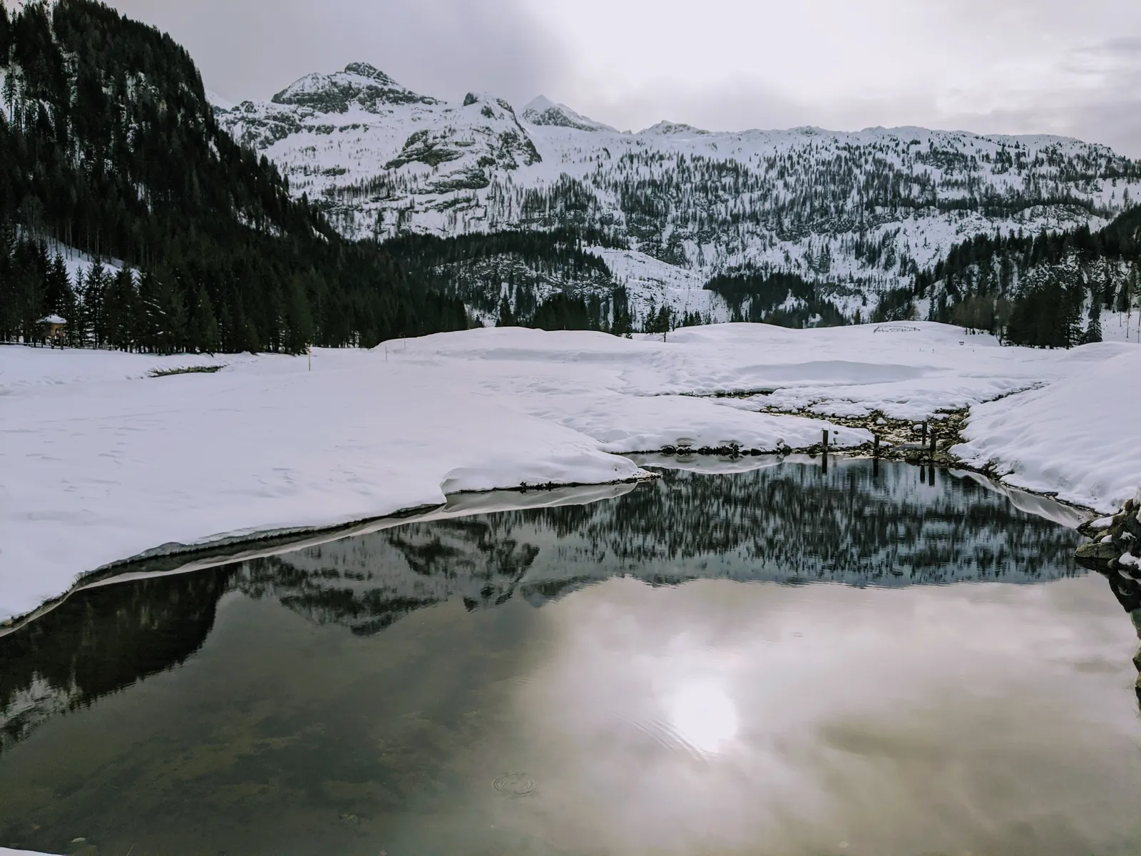 Quiet winter lake reflecting low light and snowy mountains