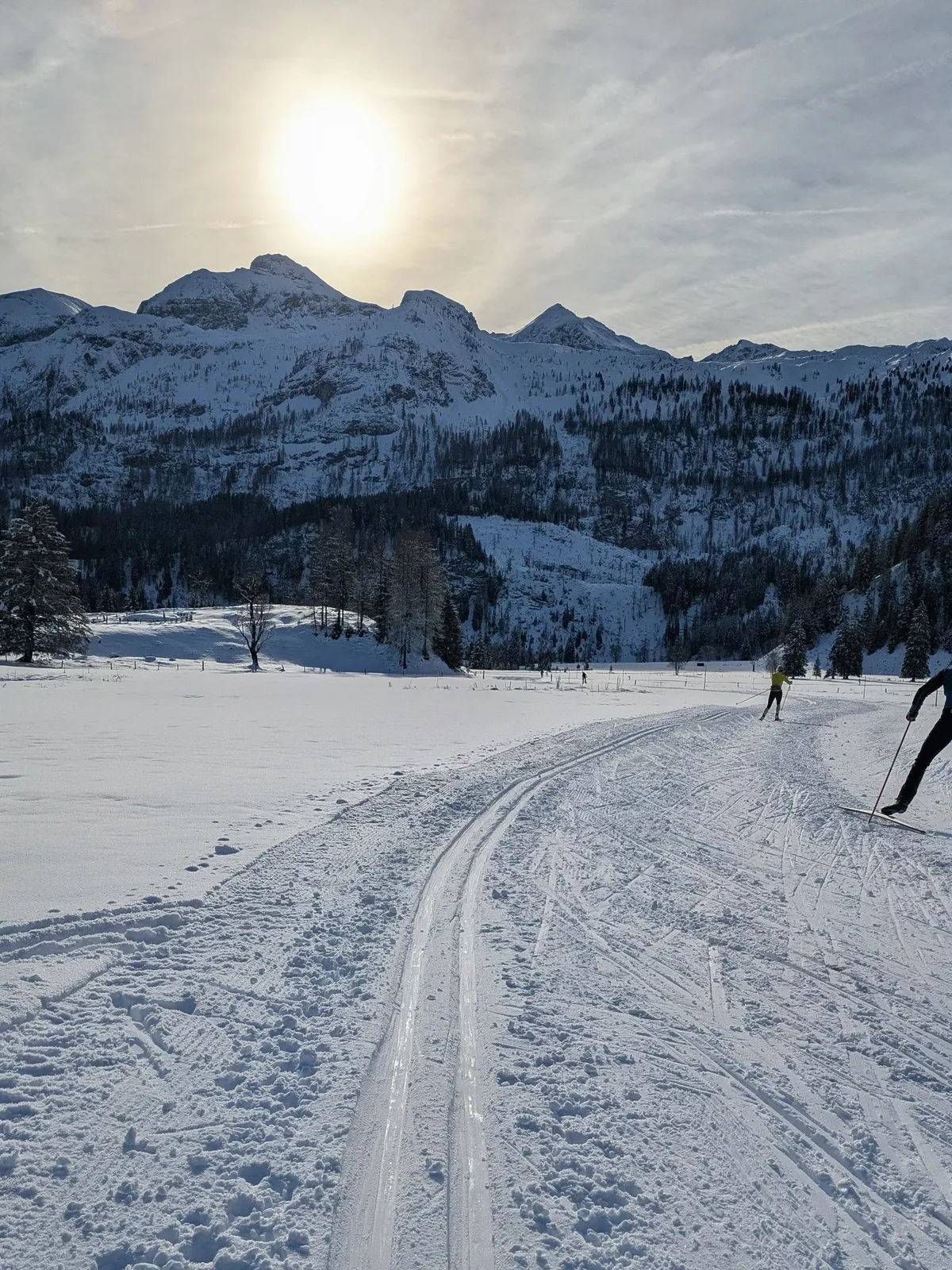 Low sun over groomed snow tracks and winter mountains